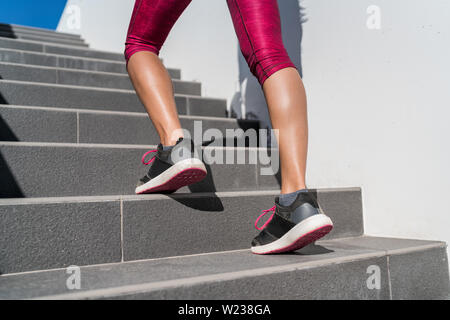 Stairs climbing running woman doing run up steps on staircase. Female runner athlete going up stairs in urban city doing cardio sport workout run outside during summer. Activewear leggings and shoes. Stock Photo