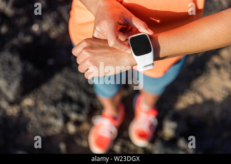 Trail runner athlete using her smart watch app to monitor fitness progress or heart rate during run cardio workout. Woman training outdoors on mountain rocks. Closeup of tech gear. Stock Photo