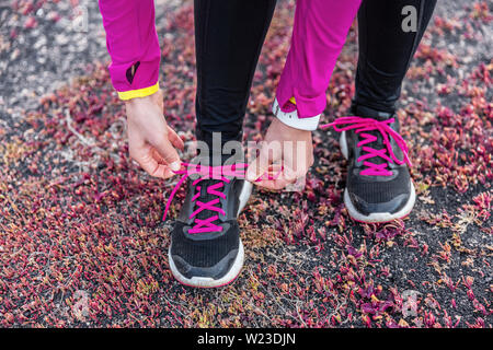 Fitness woman trail runner lacing running shoes. Athlete girl getting ready for run workout tying running shoe laces outside. Healthy lifestyle concept. Stock Photo