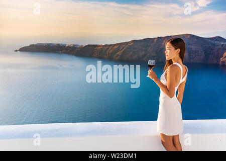 Luxury hotel terrace. Europe destination summer vacation. Asian woman drinking red wine relaxing enjoying view of the mediterranean sea in Oia, Santorini, Greece. Honeymoon high end travel holiday. Stock Photo