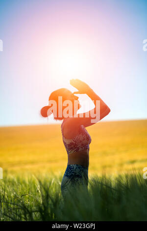 woman standing in a field meditating with sun in the sky, yoga pose. Stock Photo