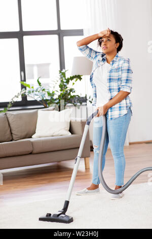 tired african woman with vacuum cleaner at home Stock Photo