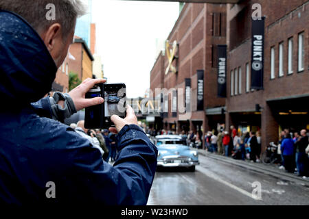 Tourist taking photos with smartphone of American cars cruising in Västerås city during Summer Meet - one of the biggest carshows in Europe Stock Photo