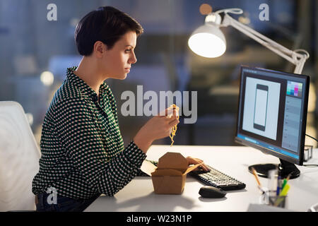 female designer eating and working at night office Stock Photo