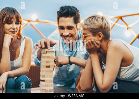 The company of young people playing jenga. Young friends at sunset on penthouse patio playing jenga Stock Photo