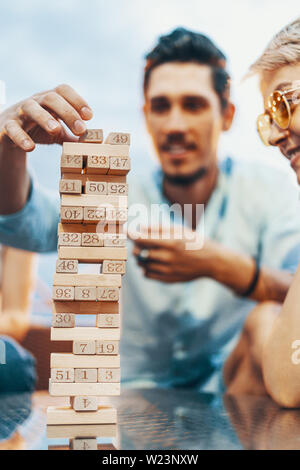 The company of young people playing jenga. Young friends at sunset on penthouse patio playing jenga Stock Photo