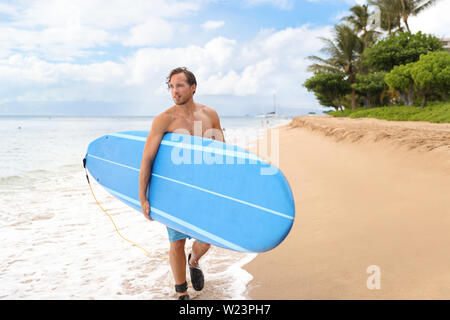 Surfer man going surfing on maui beach hawaii, usa. Professional male athlete carrying blue surf longboard going for a surf session on kaanapali beach, hawaiian destination. Travel surfer lifestyle. Stock Photo