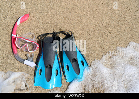 Beach vacation activity: snorkel equipment for women. Scuba diving and snorkelling. Blue Flippers, pink mask, snorkel on sandy texture background. Objects lying on sand. Stock Photo