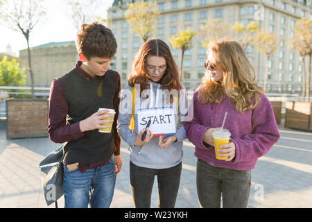 Group teenagers boy and two girls, with a notepad with handwritten word start. Teenagers looking forward, city background, golden hour Stock Photo