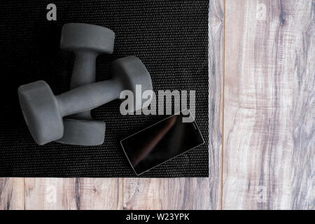 Gym fitness mat with free weights mobile phone app. Man health. Dumbbells on exercise mat and smartphone for health progress tracking app. Phone showing copy on screen for exercising videos online. Stock Photo