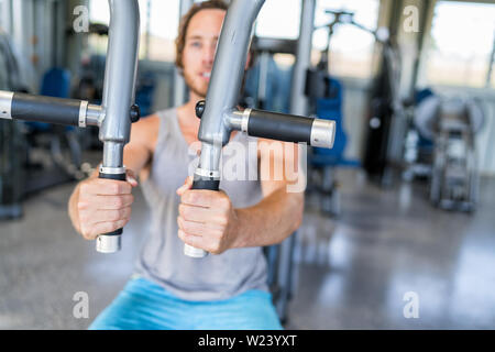 Gym machine closeup on male hands. Male athlete training chest muscles on fitness equipment pec deck fly working out strength alone indoors. Man holding handles of fitness machine at gym center. Stock Photo