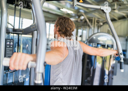 Man from behind training at fitness gym. Man doing workout on fitness machine at gym. Gym trainer athlete working out back muscles doing strength training exercises on gym benchpress equipment. Stock Photo