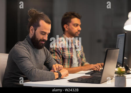 creative man with smartwatch works at night office Stock Photo