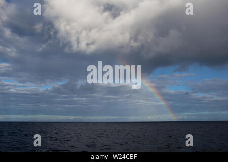 A rainbow appears over the ocean as sunlight refracts through atmospheric moisture. Rainbows are just one example of Nature's beauty. Stock Photo