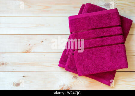 Red terry towels folded on wooden table with copy space. Top view. Soft fabric material. Indoors sauna. Close-up. Light pine-tree texture background. Stock Photo