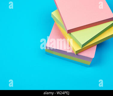 stack of multicolored empty paper square stickers on a blue background, close up Stock Photo