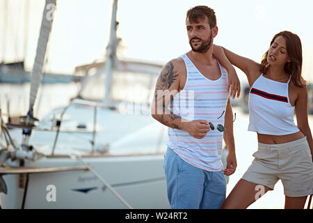 Man and woman near the yachts on the dock.  Couple in love on the dock at sunset. Stock Photo
