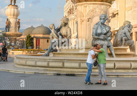 SKOPJE,NORTH MACEDONIA/AUGUST 22 2018: Two pedestrians embrace near the statues and fountains to the east side of the Stone Bridge,Skopje city center Stock Photo