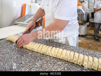 A baker a man professionally cuts with a knife in equal portions a long rolled out, stuffed and rolled again dough from organic flour and other natura Stock Photo