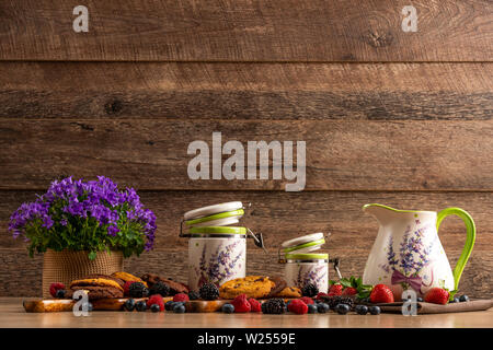 Colorful assorted mix of wild berries, violet flowers, chocolate cookies and ceramic vessels Stock Photo