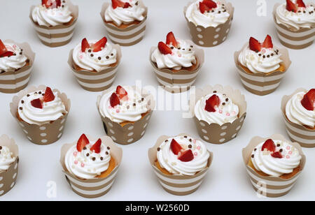 Close-up cupcakes with whipped eggs cream decorated fresh strawberry and chocolate balls on white background. Isolated top view Stock Photo