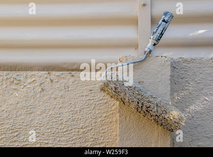 A used paint roller hangs on a concrete wall to dry out image in landscape format with copy space Stock Photo