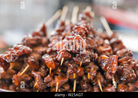 Delicious appetizing skewers of meat pieces in sweet and sour sauce, strung on wooden sticks closeup. Stock Photo