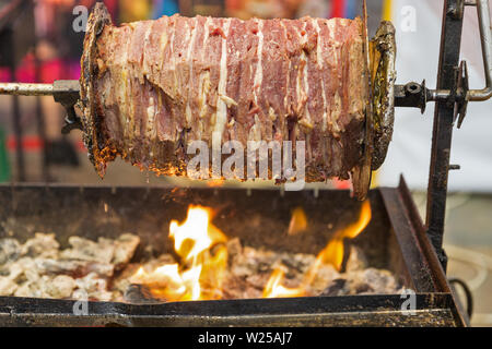 Cooking shawarma, meat layers strung on a skewer, chopped outdoors Stock Photo