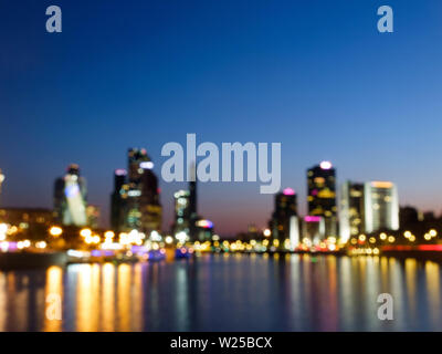 Skyscrapers and its reflections in the river captured unfocused with long exposure. Blurred lights. Soft focus. Bokeh unfocused lights in the evening Stock Photo