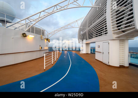 Blue treadmill for fitness on the brown upper deck of the cruise ship among the white deck structures against the cloudy sky. Stock Photo