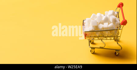 Sugar cubes. One shopping cart filled with sugar cubes on orange background. Copy space for text, panoramic image Stock Photo