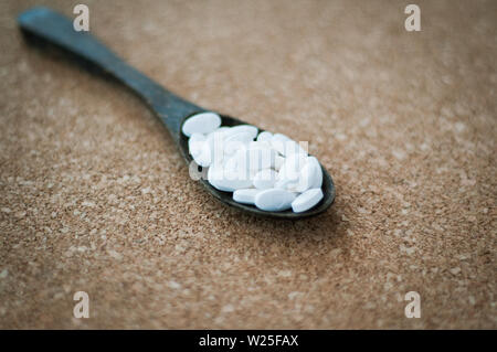 White pharmaceutical pills and medicines in the wooden spoon on a brown cork background. Valentines, heart, sick, health, and healing concept. Stock Photo