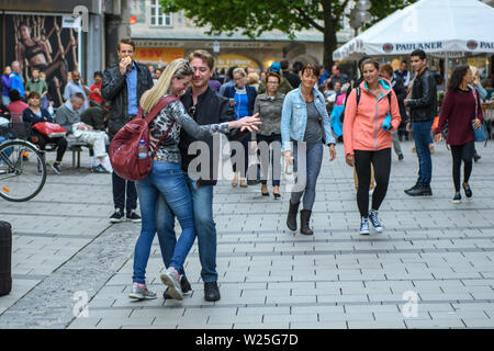 MUNICH, GERMANY - JULY, 2017: A young couple dancing a waltz in the streets of the city among the surprised passers-by Stock Photo