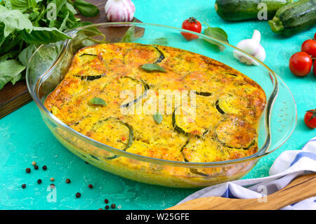 Zucchini, cheese, eggs, cream and green casserole in a transparent glass form on a bright background. Tasty healthy dish. Stock Photo