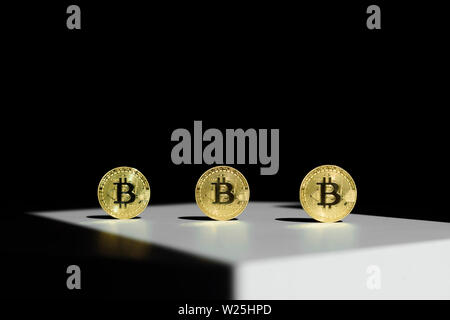 Three gold shiny coins with a bitcoin symbol in a sun ray with shadow around. Concept of business and finance in internet. Virtual crypto currency. Stock Photo