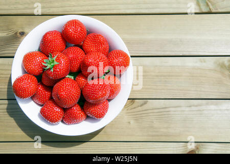 Strawberries on a wooden picnic table - summertime garden eating concept.