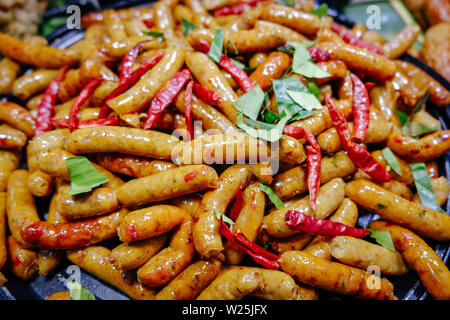 Northern Thai spicy herbal sausages freshly cooked in a pan for sale in local market, Thailand. Ready to eat street food. Stock Photo