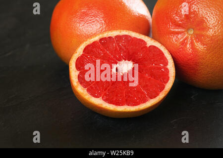 Pink grapefruit cut in half, whole citrus fruits in background on black board Stock Photo