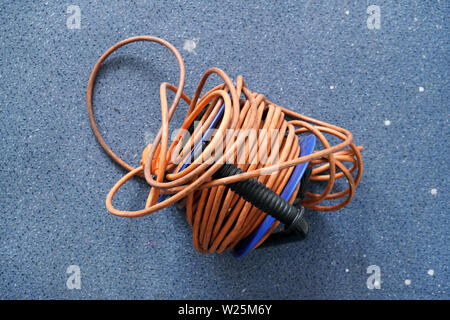 Top down view, tangled orange power cord extension lead on blue roll, over dirty carpet. Stock Photo