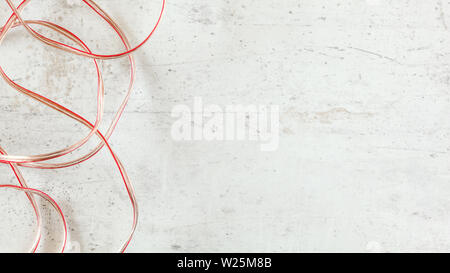 Top down view - two wires red and transparent copper speaker cable on white stone board desk, wide banner with space for text on right side Stock Photo