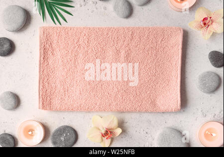 Spa concept with pink towel on white stone background, tropical orchid flowers, candle and zen like grey stones, top view, copy space. Stock Photo