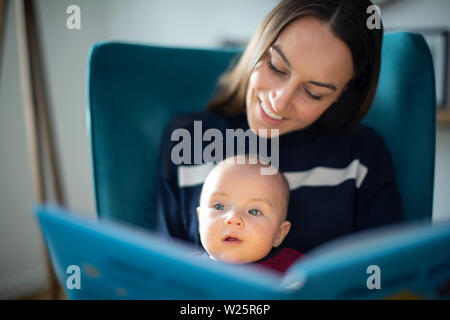 Baby Son Sitting On Mothers Lap Reading Story Book Together Stock Photo
