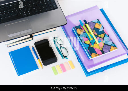 School stationery accessories - notebook, copybook, laptop, plastic folder, pens, glasses, paper clips, stickers, notepads, smartphone, stack of books Stock Photo