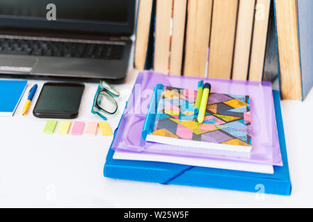 School stationery accessories - notebook, copybook, laptop, plastic folder, pens, glasses, paper clips, stickers, notepads, smartphone, stack of books Stock Photo