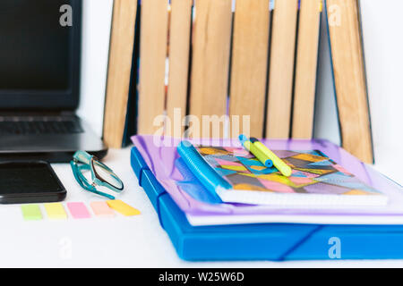 School stationery accessories - notebook, copybook, laptop, plastic folder, pens, glasses, paper clips, stickers, notepads, smartphone, stack of books Stock Photo