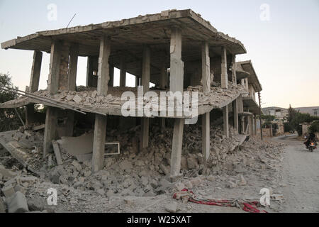 Muhambal, Syria. 06th July, 2019. People ride a motorcycle ride past a building that was destroyed in an airstrike, allegedly carried out the day before by the Syrian government on the town of Muhambal in the rebel-held Idlib Province. Credit: Anas Alkharboutli/dpa/Alamy Live News Stock Photo