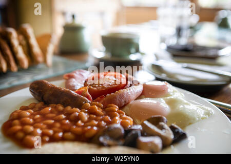 traditional British and Scottish breakfast with egg, beans, tomato, mushroom and haggis served on a white plate, standing on a table with a blurred ba