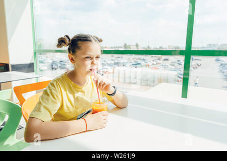 A teenager girl sits in a cafe drinking a carrot smoothie Stock Photo