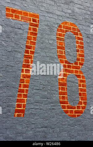 House number 78 with the seventy-eight painted inversely as a gray outline on a red brick wall seen at an angle Stock Photo