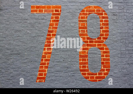 House number 78 with the seventy-eight painted inversely as a gray outline on a red brick wall Stock Photo